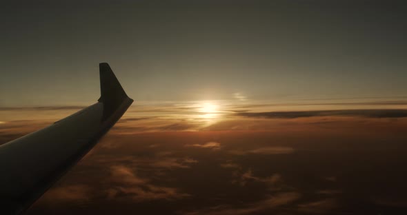 Wing of an Airplane Flying Above the Clouds with Sunset Sky, View From the Window of the Plane alt