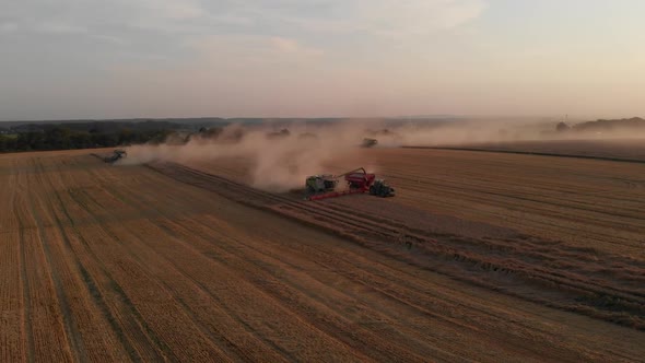 Aerial drone shot: combine harvesting wheat pouring harvested wheat into tractor tipper.