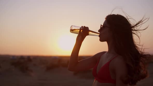 Beautiful Young Hipster Woman in Bikini Drinking Beer at Sunset