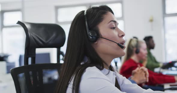 Woman wearing headset talking while sitting on her desk at office alt