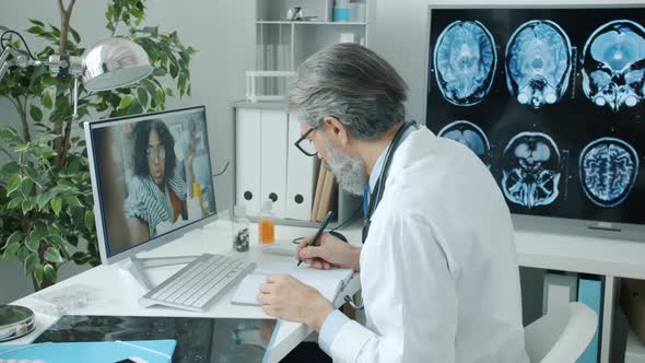 Experienced Doctor in White Coat Consulting Female Patient During Video Call From Hospital alt