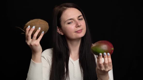 Woman Shows Coconut and Mango in Hands on a Black Background alt
