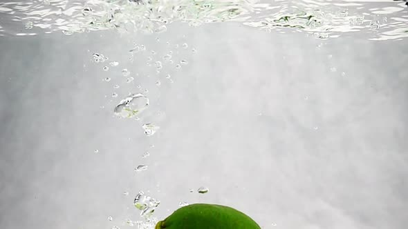 Green Limes Are Thrown Into a Container of Water. Video of Fruit in Slow Motion alt