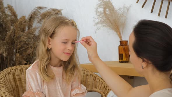Young Mother Applying Makeup on Daughter Indoors alt