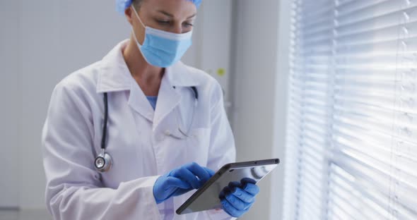 Caucasian female doctor wearing face mask and surgical gloves using tablet alt