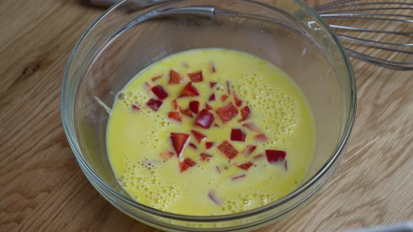 Chef whisking eggs with red pepper and green dill in bowl to make an omelette alt