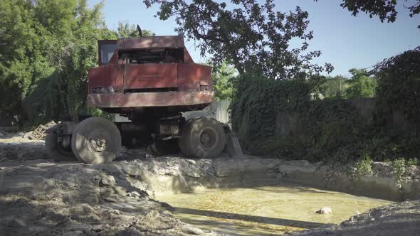 Wide Shot of Abandoned Industrial Truck Standing Over Polluted Paddle in Sunlight. Neglected alt