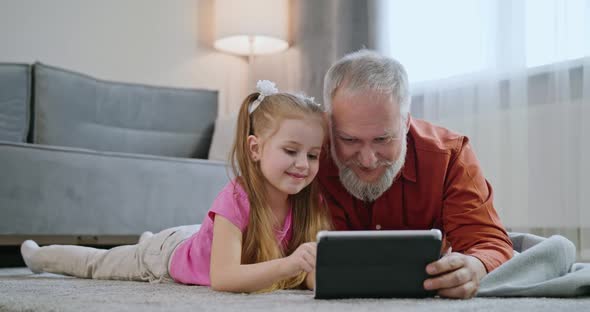 Happy Family Adult Parent Dad and Small Daughter Having Fun Using Digital Tablet Lying on Floor at