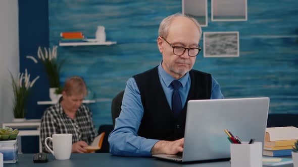 Retired Manager Sitting at Desk in Front of Camera Smiling alt