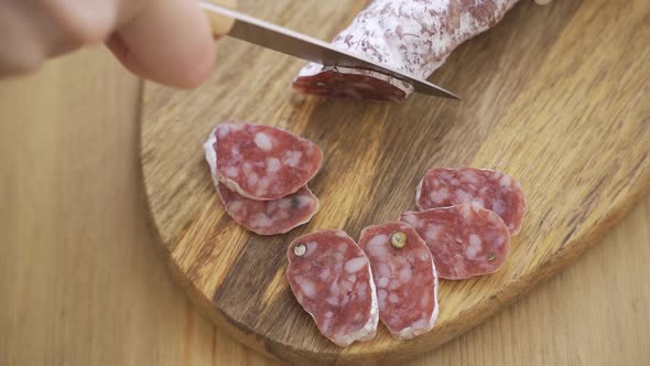 Chef Slices Spanish Traditional Homemade Choriso Sausage Into Pieces on a Wooden Cutting Board alt