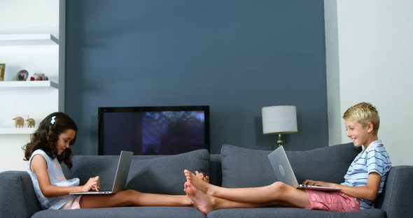 Siblings using laptop in living room alt