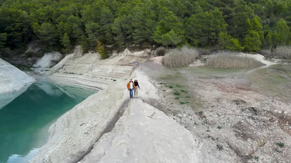 Couple Walks By Stony Lake Shore By Forest in Spain Aerial Pushout alt
