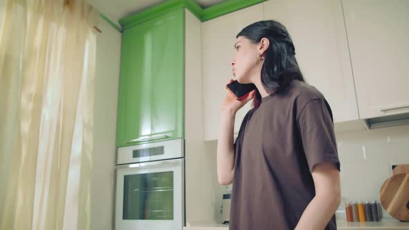 Young Woman in Brown Tshirt Speaking By Cell Phone and Looking Throw a Window