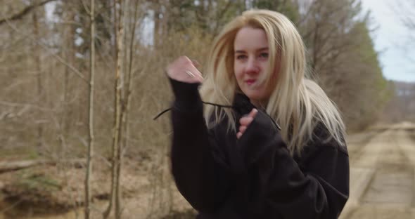 a girl with loose hair beats with her fists vered boxing then laughs in the forest alt