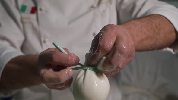 Italian Chef at a Factory Ties a Knot with a Ribbon on Dairy Mozzarella Cheese