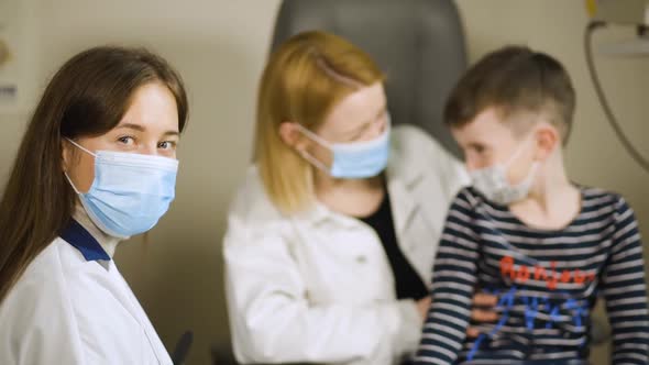 Female Eye Doctor in Medical Face Mask Patients Talking Behind. Hello in French on Sweater alt