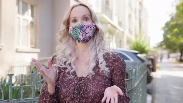 A Middleaged Caucasian Woman in a Face Mask Talks to the Camera in an Urban Area alt
