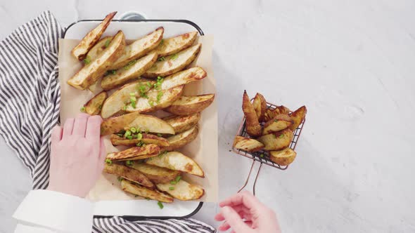 Flat lay. Freshly baked potato wedges with spices on a white serving tray alt
