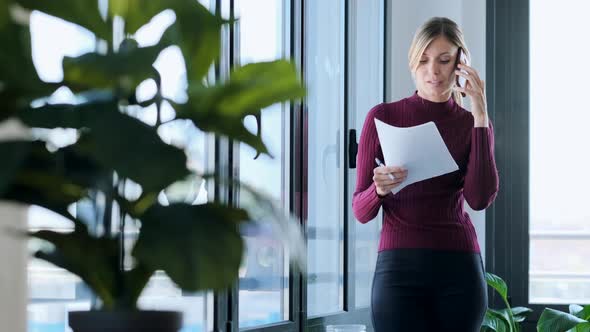 Businesswoman using smartphone and looking out of the window in office alt