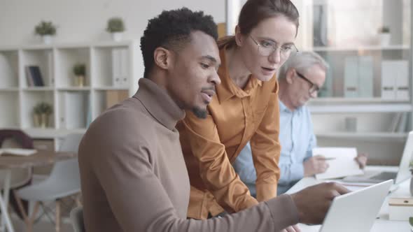 Two Creative Multiethnic Colleagues Discussing Project on Laptop Screen alt