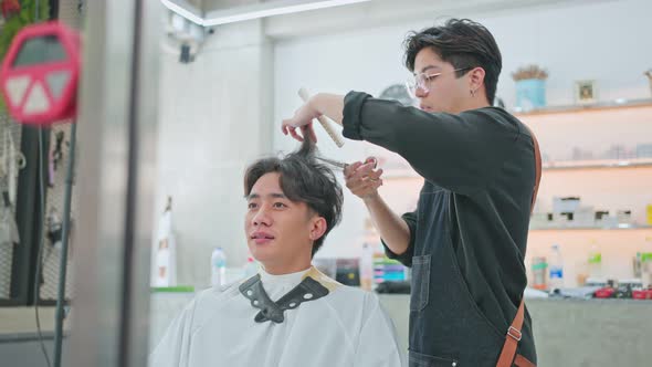 Asian professional male hairstylist combing and using scissors cutting young customer's hair. alt