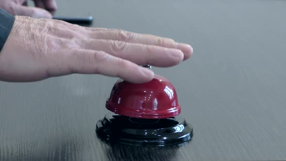 A man's hand rings a bell at the front desk.