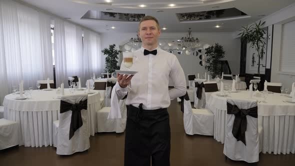 Man in Apron Carrying Tray with Cup of Latte for Customer in Cozy Cafeteria alt