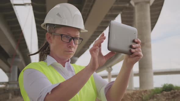 Serious female engineer or inspector in white hard hat working on tablet computer alt
