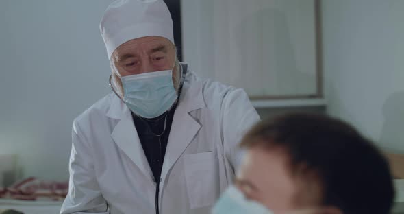 Older Doctor Sits and Cares Sick Patient Coughing From Coronavirus in Hospital alt