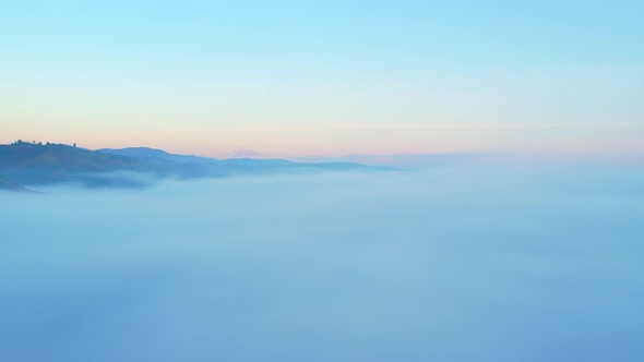 4K aerial view over mountain at sunrise in heavy fog. golden morning sunlight alt