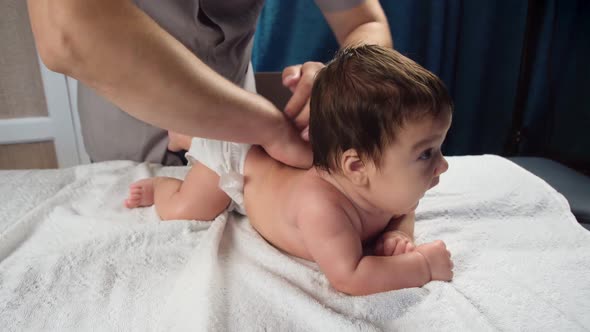 Male Doctor's Hands Massage the Baby. A Child Who Is Being Massaged Is Lying on the Couch. Back alt