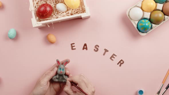 Hand of a Man is Painting a Little Rabbit with Easter Background alt