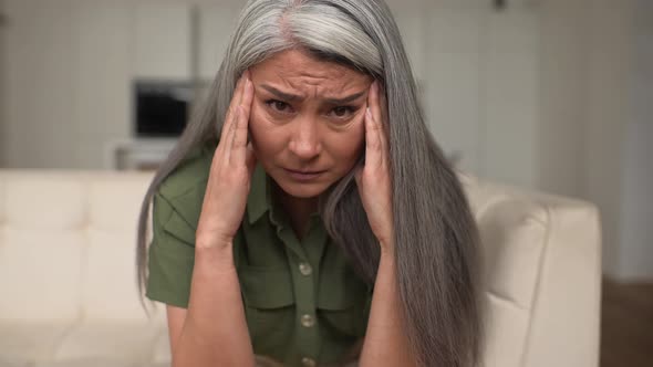 Middleaged Woman with Long Silver Hair Rubbing Temples Suffering From Migraine