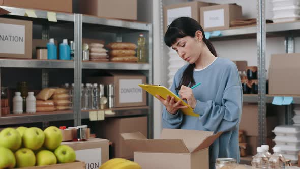 Woman with Clipboard in Hands Volunteering at Warehouse alt