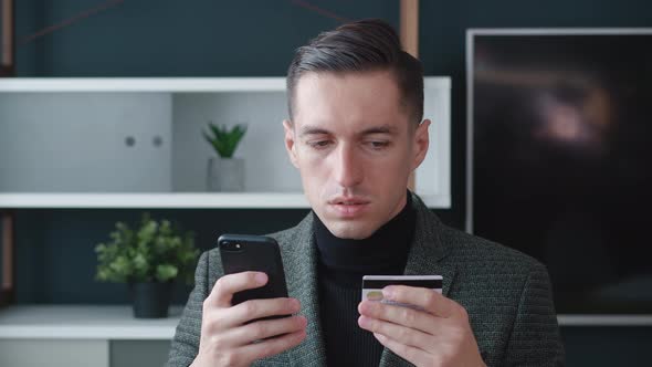 Young Businessman Shopping Online on His Smartphone and Paying with Credit Card at Modern Office