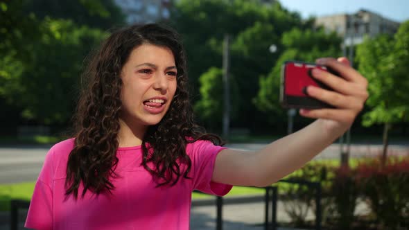 Happy Mixed Race Girl Pink Tshirt Talks Via Video Link on Smartphone City Park alt