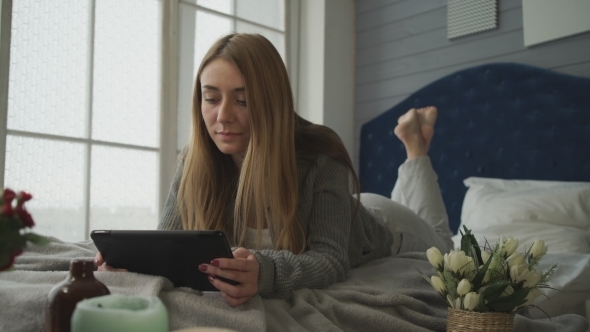 The Woman Lying On a Bed With a Tablet