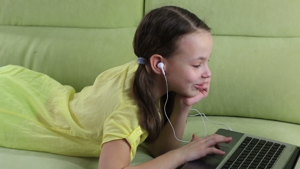 Beautiful Little Girl Lying On The Couch And Watching Movie On Laptop alt