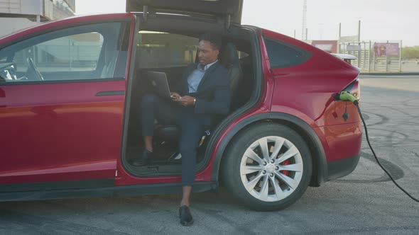 Confident Male Entrepreneur Sitting Inside His Luxury Red Car with Opened Door alt