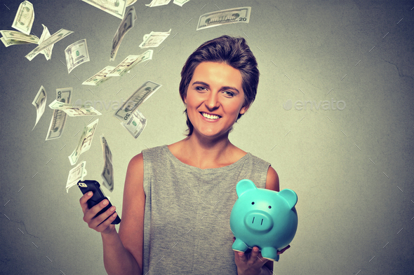 Happy woman with piggy bank and smart phone dollar banknotes bills flying away