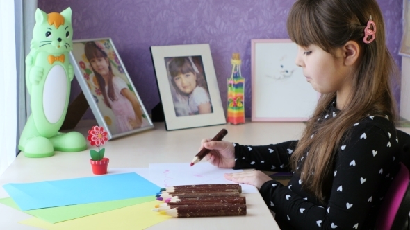 A Young Girl Draws a Heart On Paper With a Pencil alt