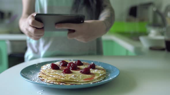 Woman makes photo of cooked pancakes served on blue plate