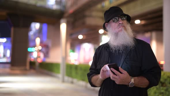 Mature Bearded Tourist Man Using Phone in the City Streets at Night