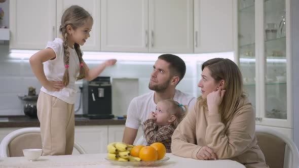 Funny Little Girl Standing on Chair Talking and Gesturing Scolding Couple of Parents and Sister alt