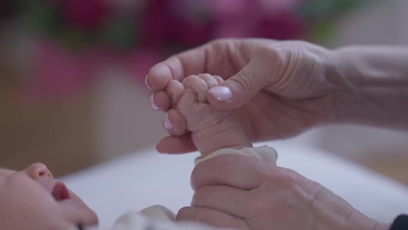 Closeup Female Caucasian Hand Caressing Fist of Newborn Crying Girl Indoors alt