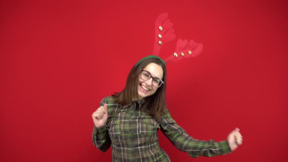 A Young Woman Is Dancing with a Headband in the Form of Christmas Antlers. Studio Shooting on a Red alt