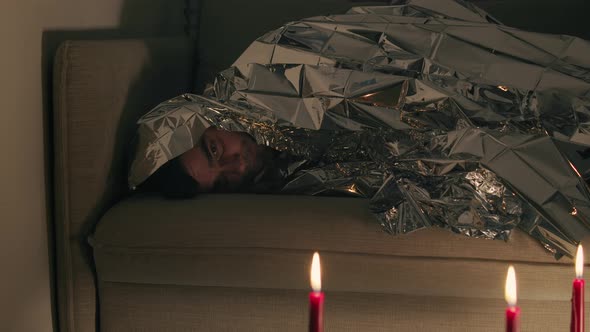 Man covered by a foil blanket looking on candles