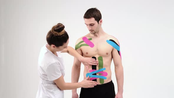 Female therapist applying kinesiology tape on a man's abdomen on the light background alt