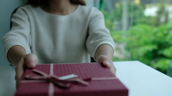 Closeup of a young woman receiving and opening a red present box