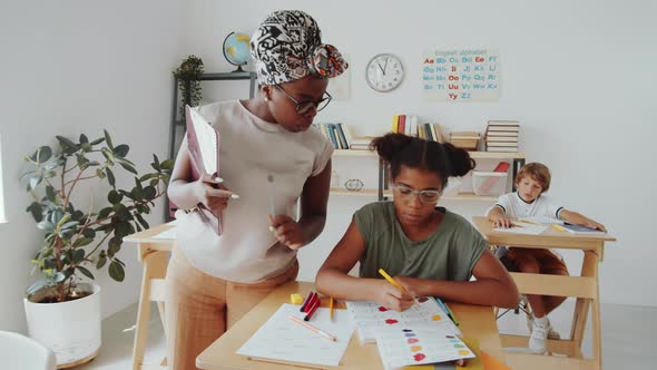 Afro-American Teacher Helping Children during Lesson in Primary School alt
